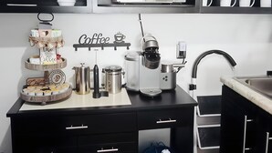 Une cuisine moderne avec des meubles de rangement sombres, un four à micro-ondes encastré, une machine à café et un distributeur d’eau.