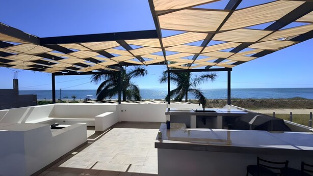 Une terrasse extérieure moderne avec vue sur l’océan, comprenant un espace salon et un bar.