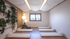 A room with a wooden floor, four white mats, a window with a city view, a hanging plant, and a wall-mounted light fixture. - Vila Olimpia Viva Benx Flats by Feel Sampa (São Paulo)