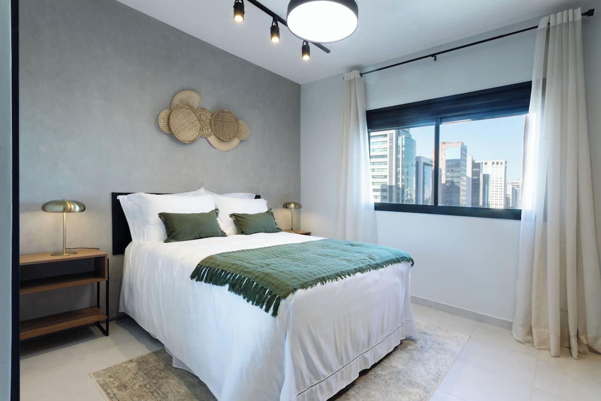 Ein modernes Schlafzimmer mit einem großen Bett, zwei Nachttischen, Blick auf die Stadt und einer Deckenleuchte.