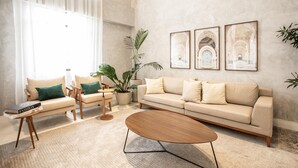 A modern living room with a beige sofa, a wooden coffee table, and a large window with sheer curtains. There are three framed pictures on the wall and several potted plants. - Vila Olimpia Viva Benx Flats by Feel Sampa (São Paulo)