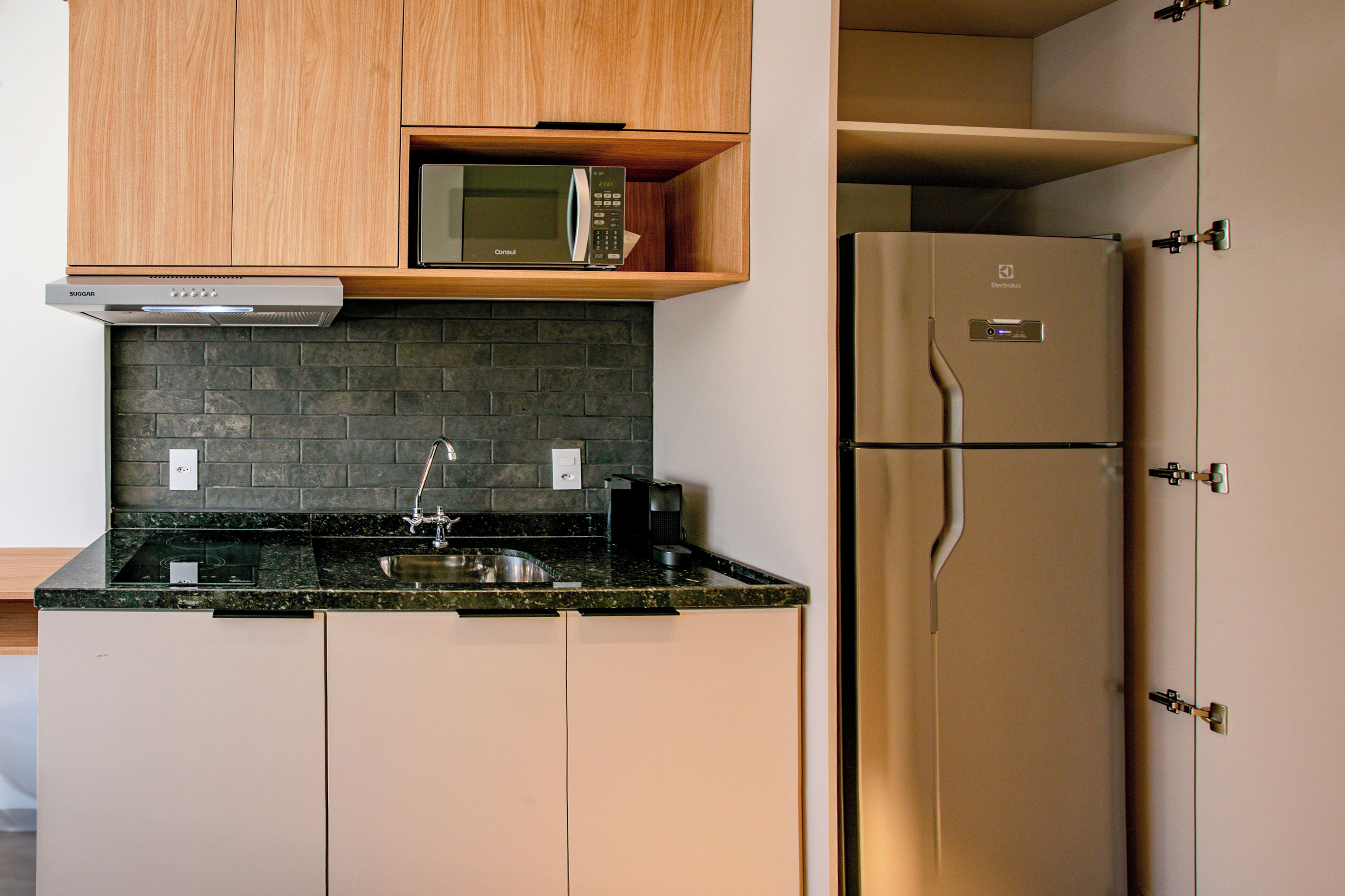 Una cocina moderna con microondas integrado, refrigerador de acero inoxidable, encimera de granito y salpicadero de ladrillo.