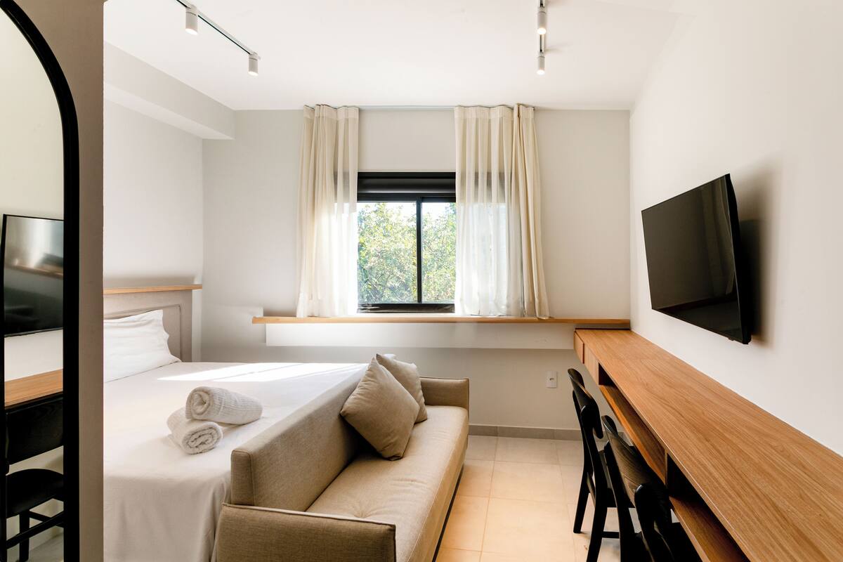 Ein modernes Hotelzimmer mit Bett, Sofa, Schreibtisch und einem an der Wand befestigten Fernseher.