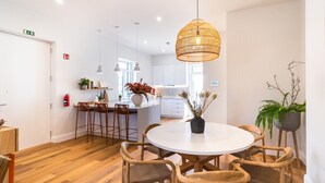 Een moderne keuken met witte kastjes, een ronde eettafel met rieten stoelen en een hanglamp.