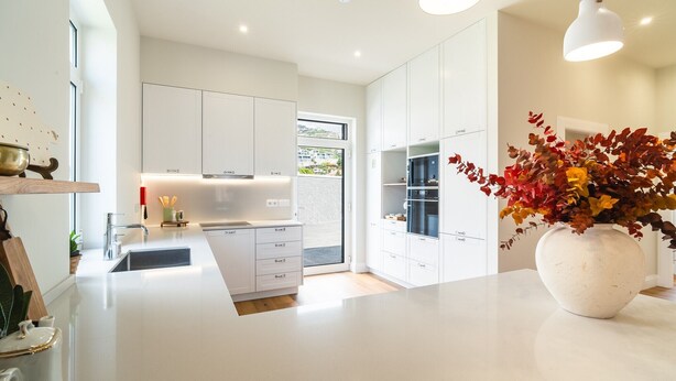 Een moderne keuken met witte kasten, een groot eiland en een vaas met herfstbladeren.