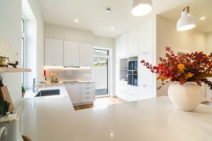 Une cuisine moderne avec des meubles blancs, un grand îlot central et un vase rempli de feuilles d’automne.