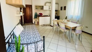A compact room with a bed, a dining table with chairs, a kitchenette, and a small bathroom.