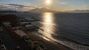 Un paisaje urbano costero con una montaña destacada al fondo, cielo despejado y un mar tranquilo que refleja el sol.