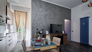 A modern kitchen with a dining area, featuring a large window, a flat-screen TV, and a blue radiator. - City Center Suite (Milan)