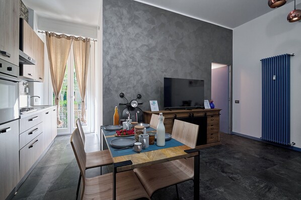 A modern kitchen with a dining area, featuring a large window, a flat-screen TV, and a blue radiator. - City Center Suite (Milan)