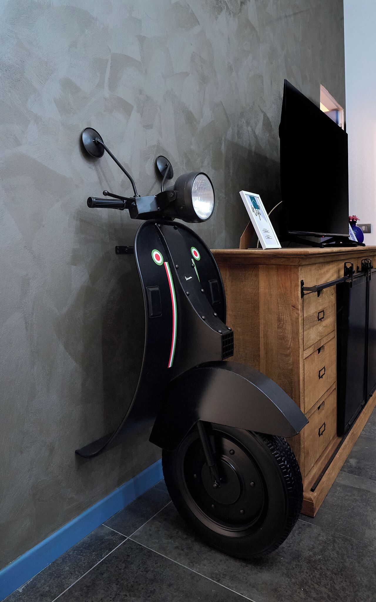 A scooter parked against a wall with a wooden cabinet and a television in the background.