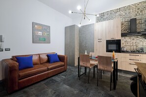 Une cuisine moderne dotée d’un four et d’un micro-ondes encastrés, un coin repas avec une table et des chaises en bois, et un canapé en cuir marron agrémenté de coussins bleus.