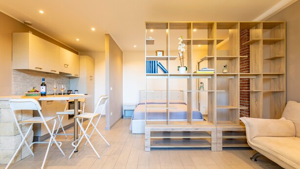A modern interior with a kitchen, dining area, and a living space with a sofa and bookshelves.