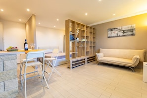Un salon moderne avec un canapé, un coin repas avec des chaises, une bibliothèque en bois et un tableau accroché au mur.