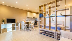 A modern living room with a TV, seating area, and a kitchen in the background.