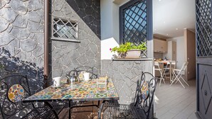 A patio with a stone wall, a tiled table, metal chairs, and a potted plant.