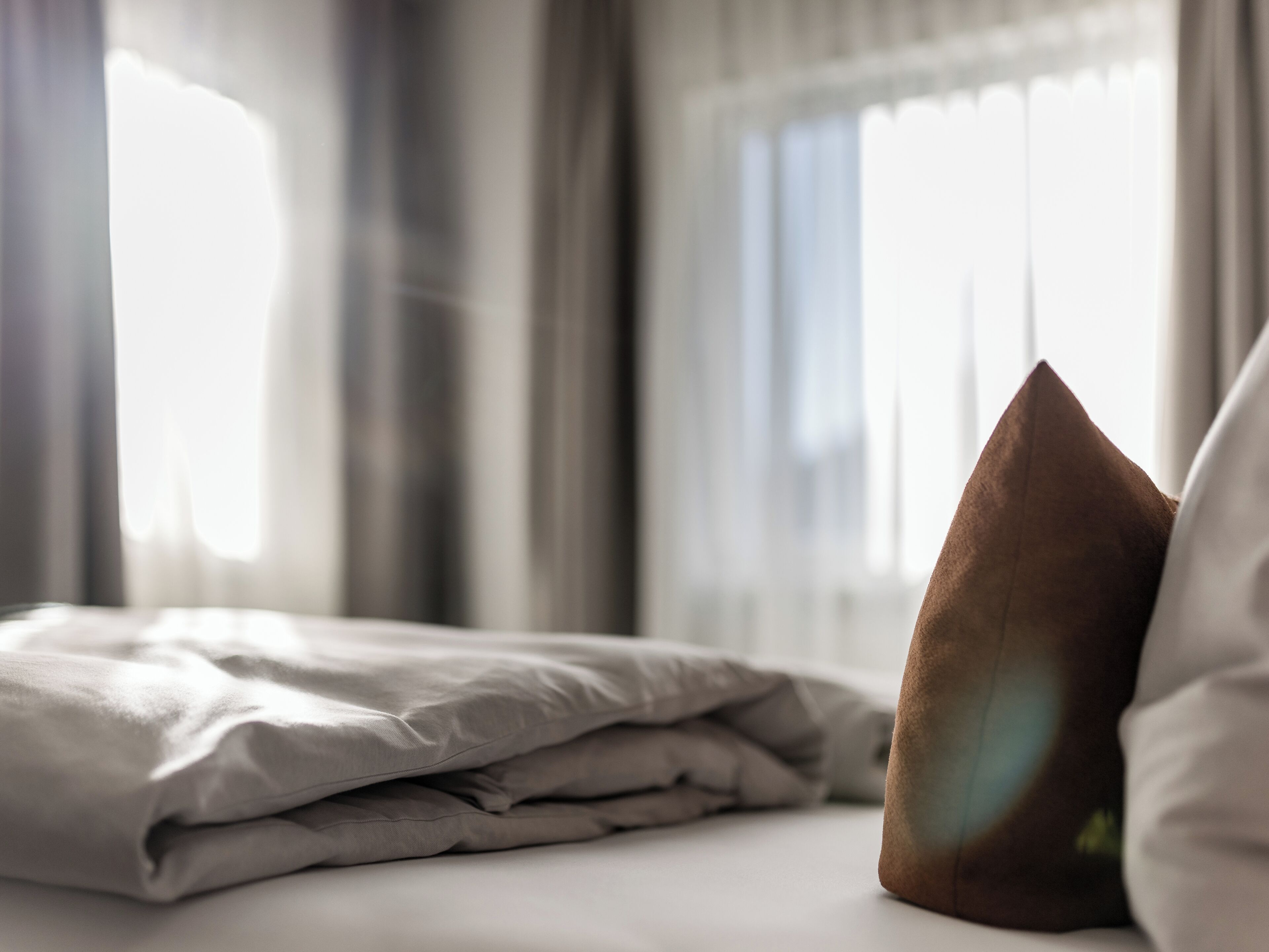 A neatly made bed with a folded blanket and a brown pillow.