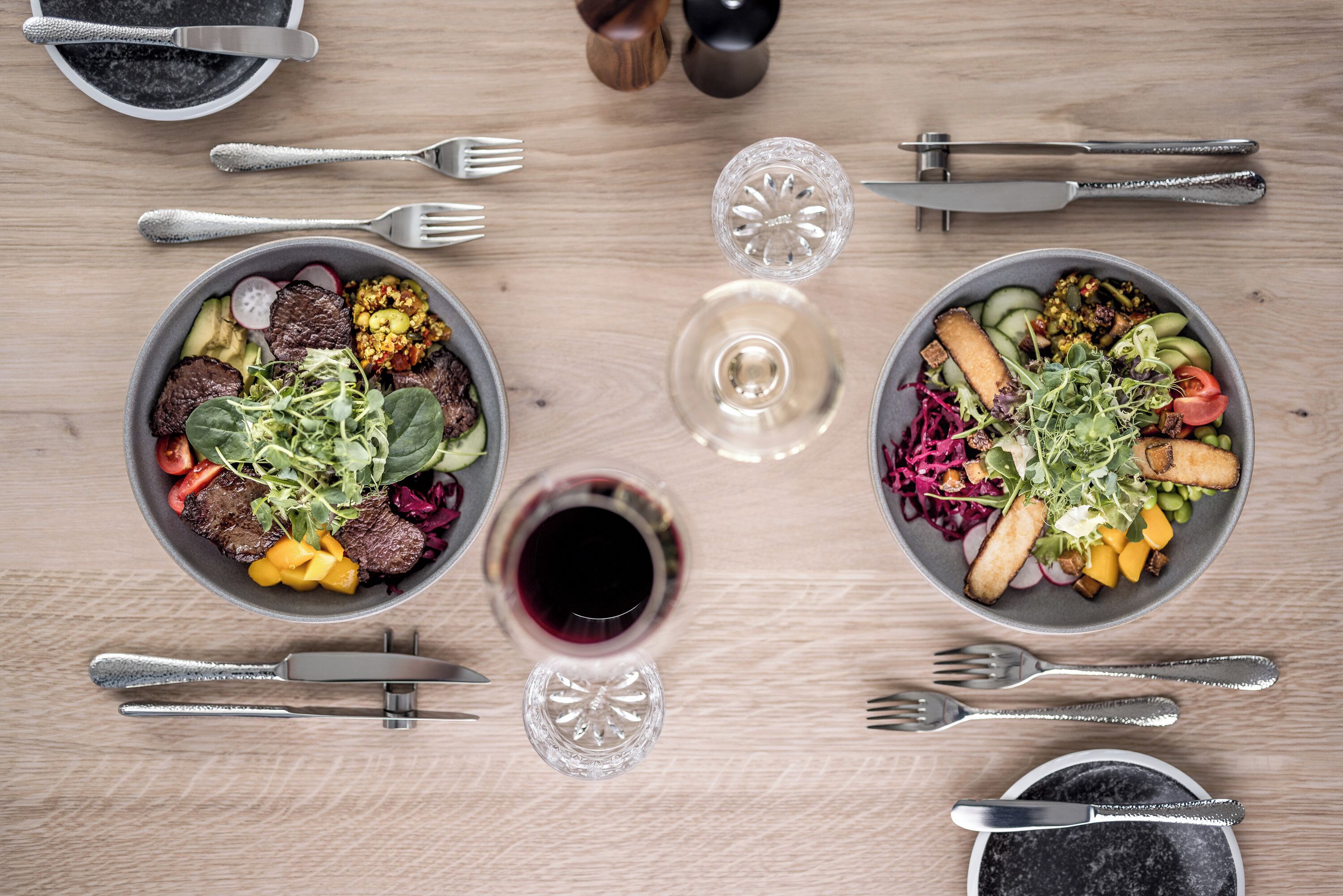 Twee kommen eten en een glas rode wijn op een houten tafel.