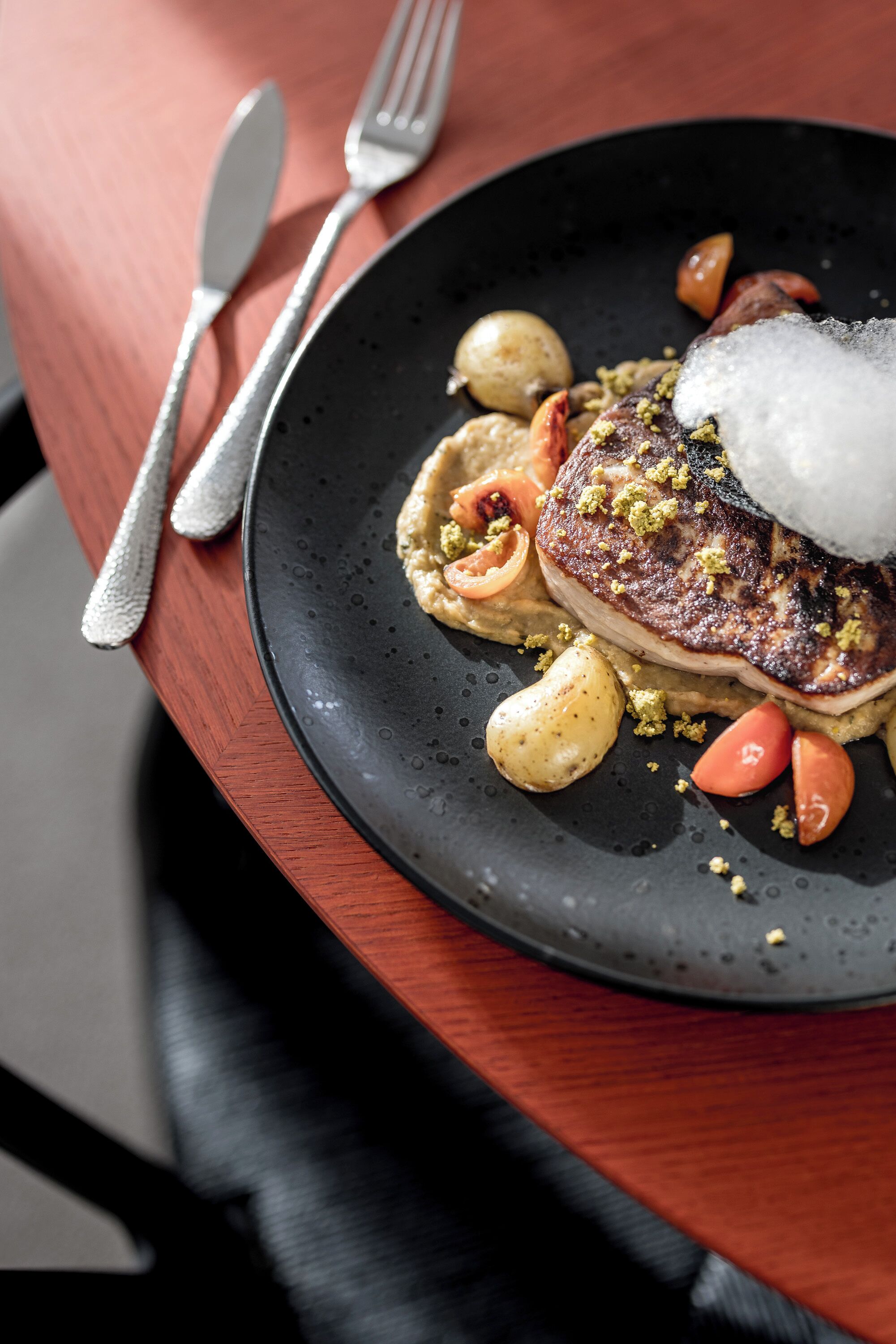 Une assiette contenant un steak, des pommes de terre et des légumes, le tout présenté sur une assiette foncée.
