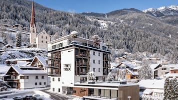Un hotel moderno con restaurante, bar y jardín gastronómico, rodeado de edificios nevados y montañas.
