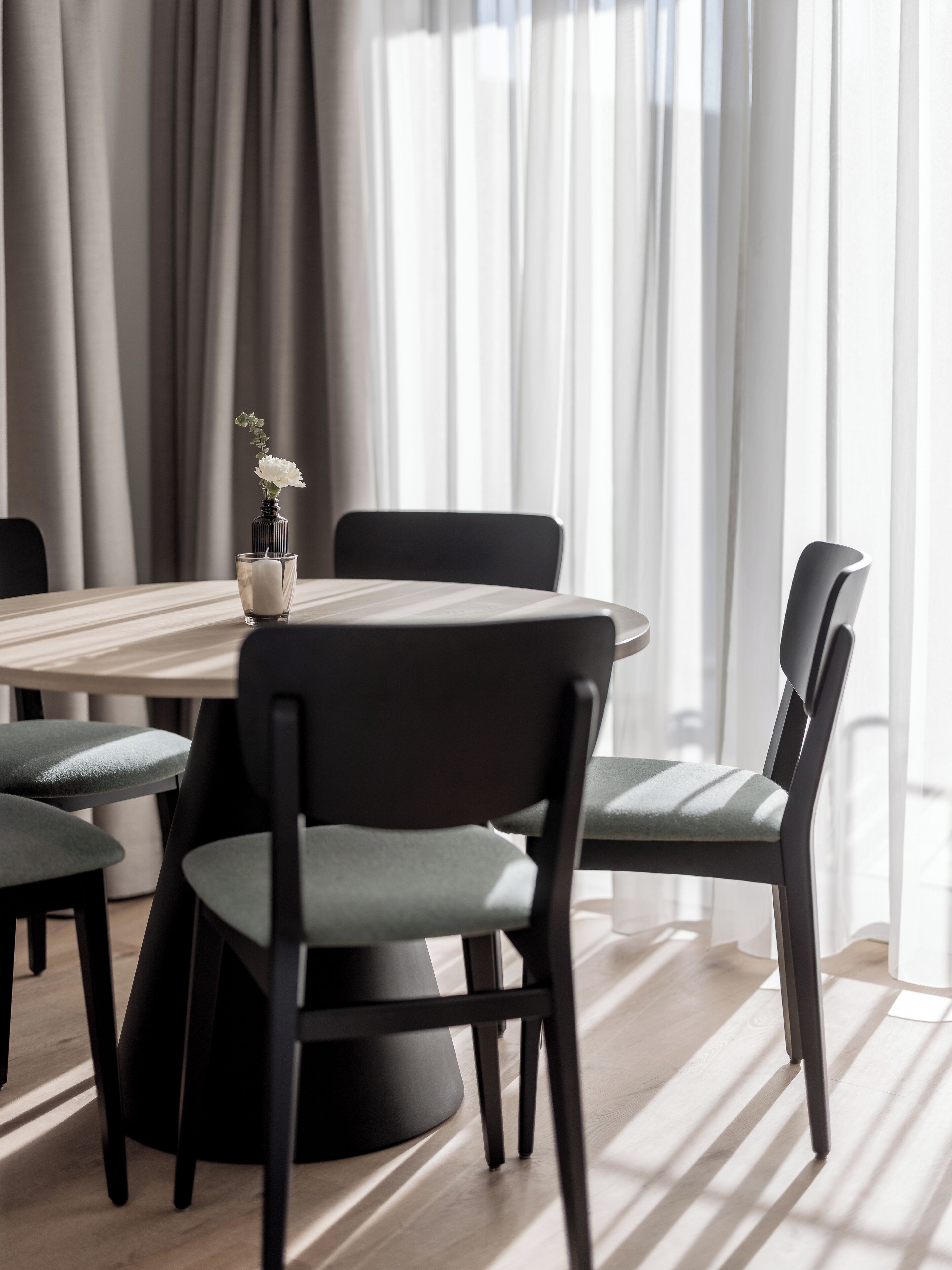 A modern dining area with a round table, black chairs, and a vase with flowers.