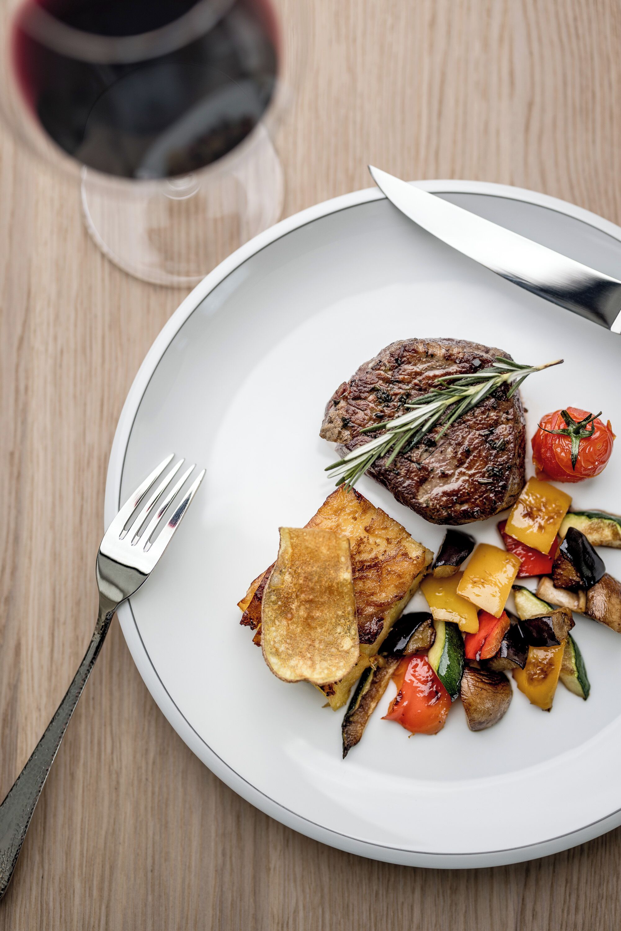 Un plato con bistec, verduras y una copa de vino tinto.