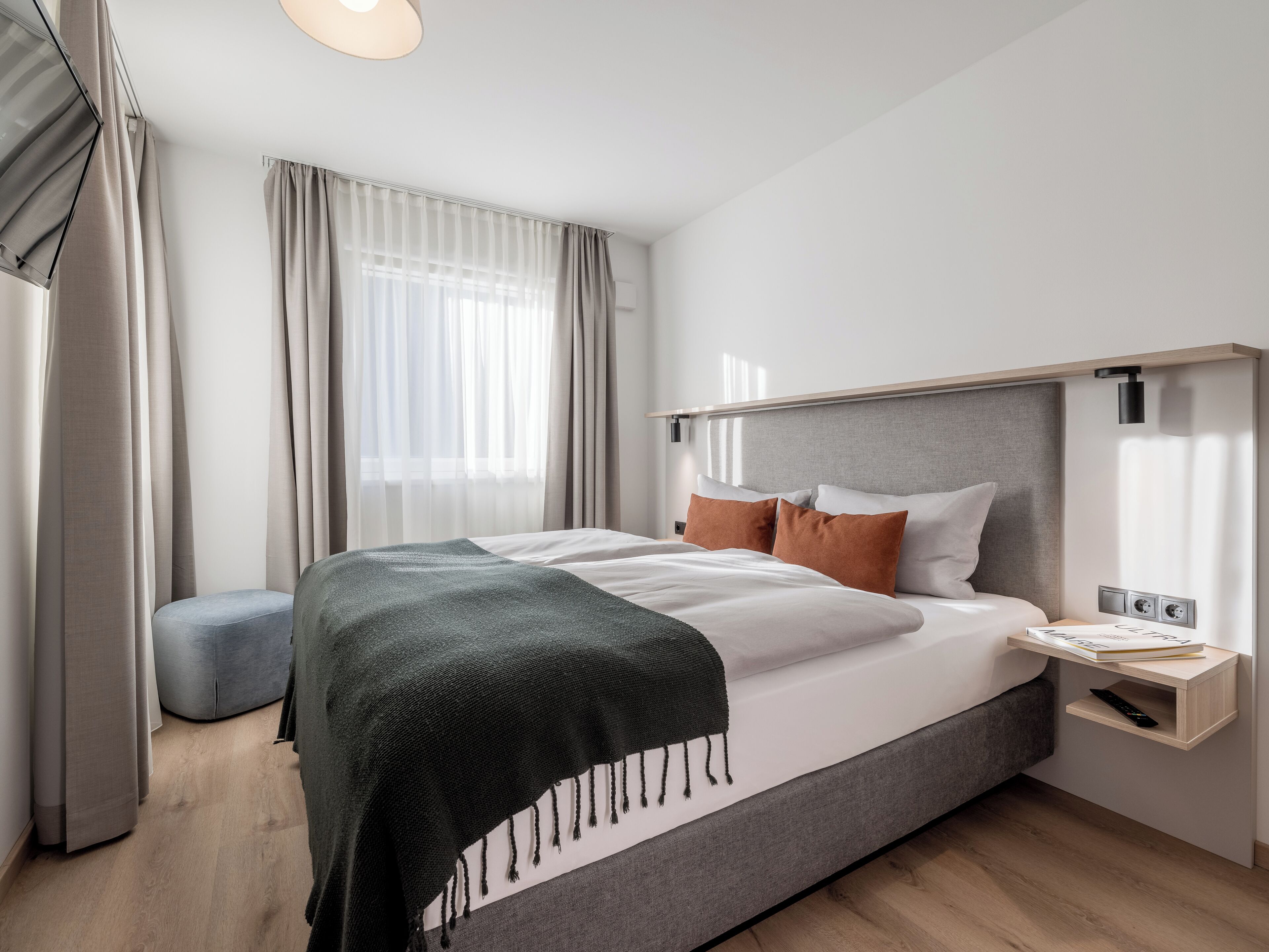 Een moderne hotelkamer met een groot bed, een nachtkastje met lamp en een raam met dunne gordijnen.