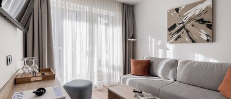 A modern living room with a sofa, a coffee table, a side table, a magazine, and a tray with wine glasses.