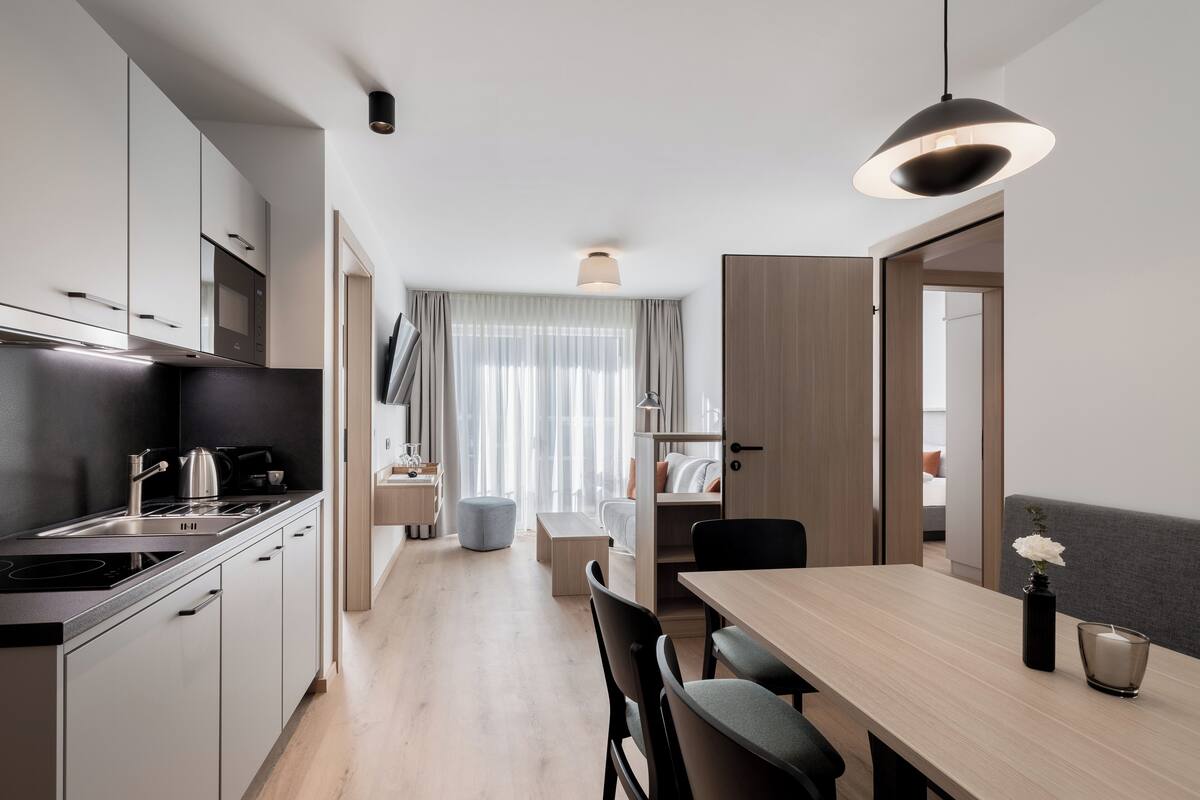A modern kitchen with a dining area, wooden cabinets, and a large window with curtains.