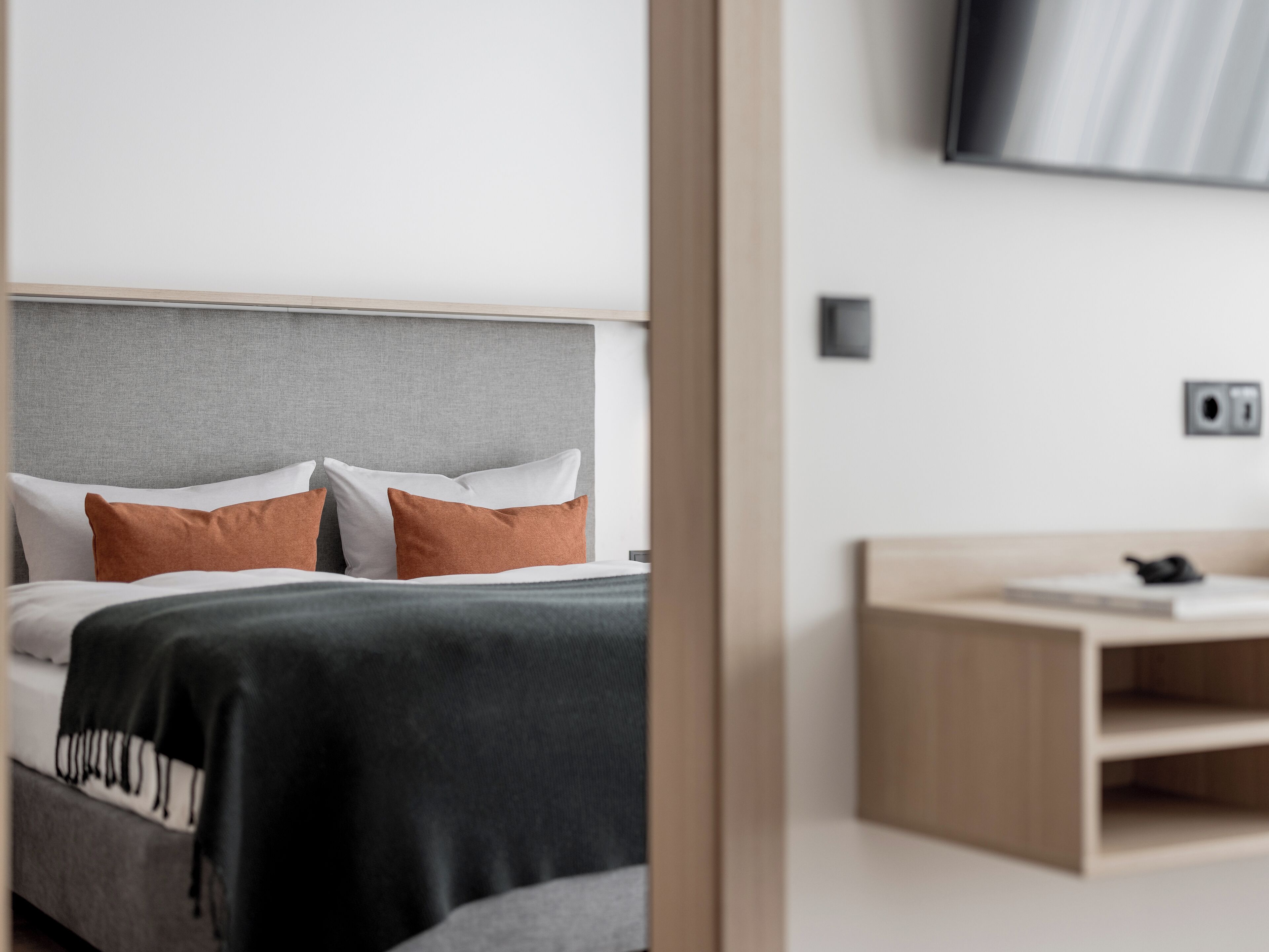 Un dormitorio moderno con una cama, una mesita de noche y un televisor montado en la pared.