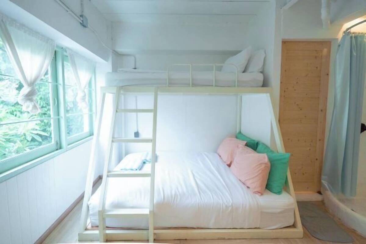Una habitación con literas, una escalera, una ventana con cortinas y una puerta.