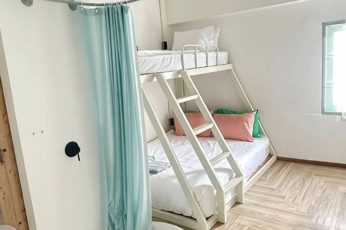 Una cama litera con escalera, ventana y cortina.