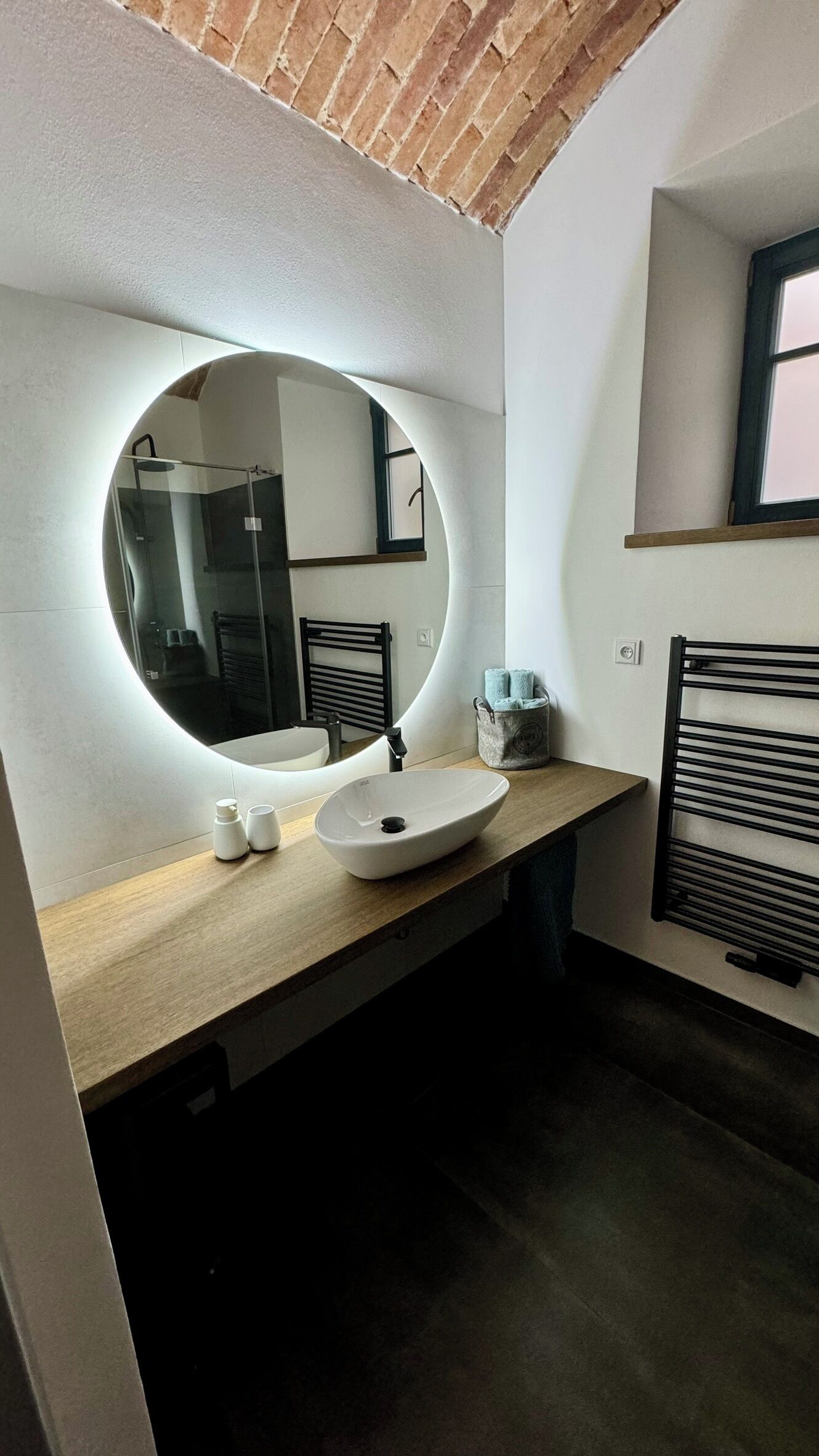 A modern bathroom with a round mirror, a sink, and a towel rack.
