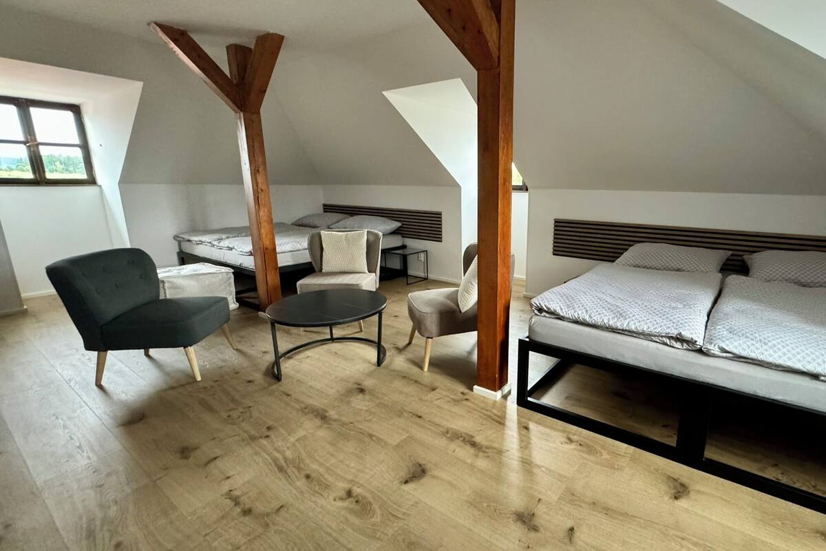 A loft bedroom with a bed, two chairs, a small table, and wooden beams.