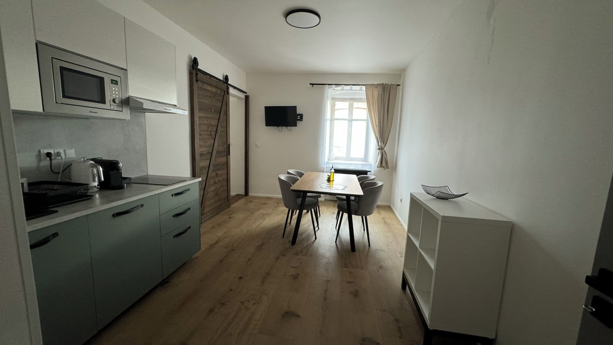 Cocina compacta con microondas, tostadora y hervidor. Hay una mesa de comedor con sillas y un refrigerador pequeño.