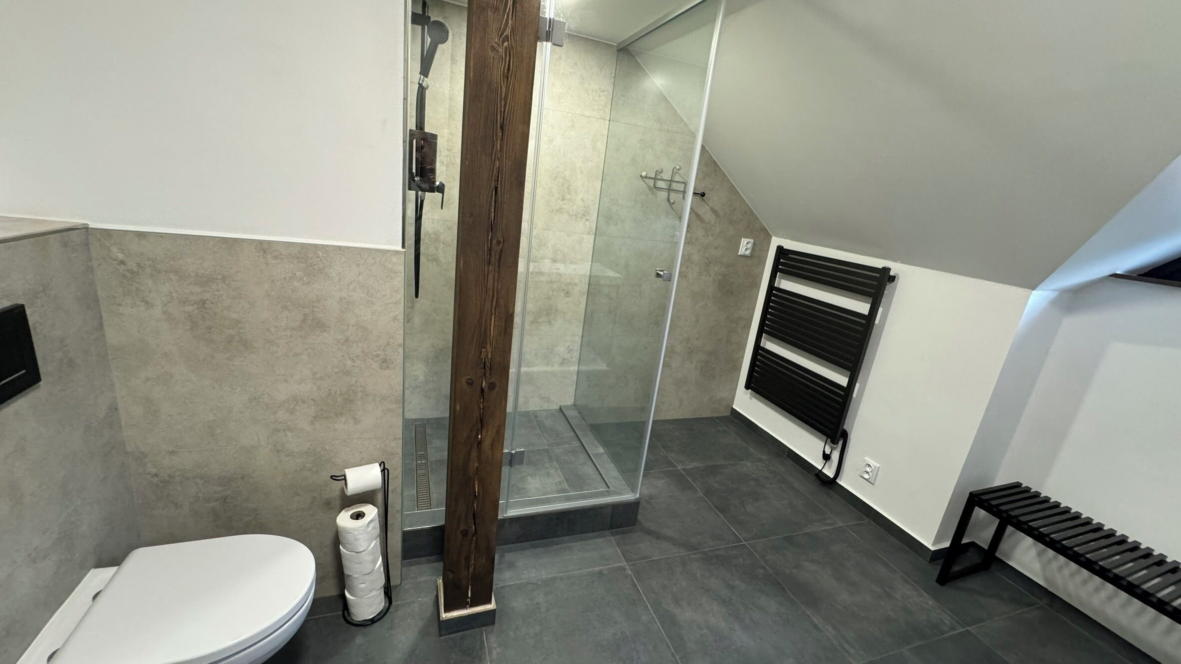 Een moderne badkamer met een douchecabine van glas, een toilet en een bankje.