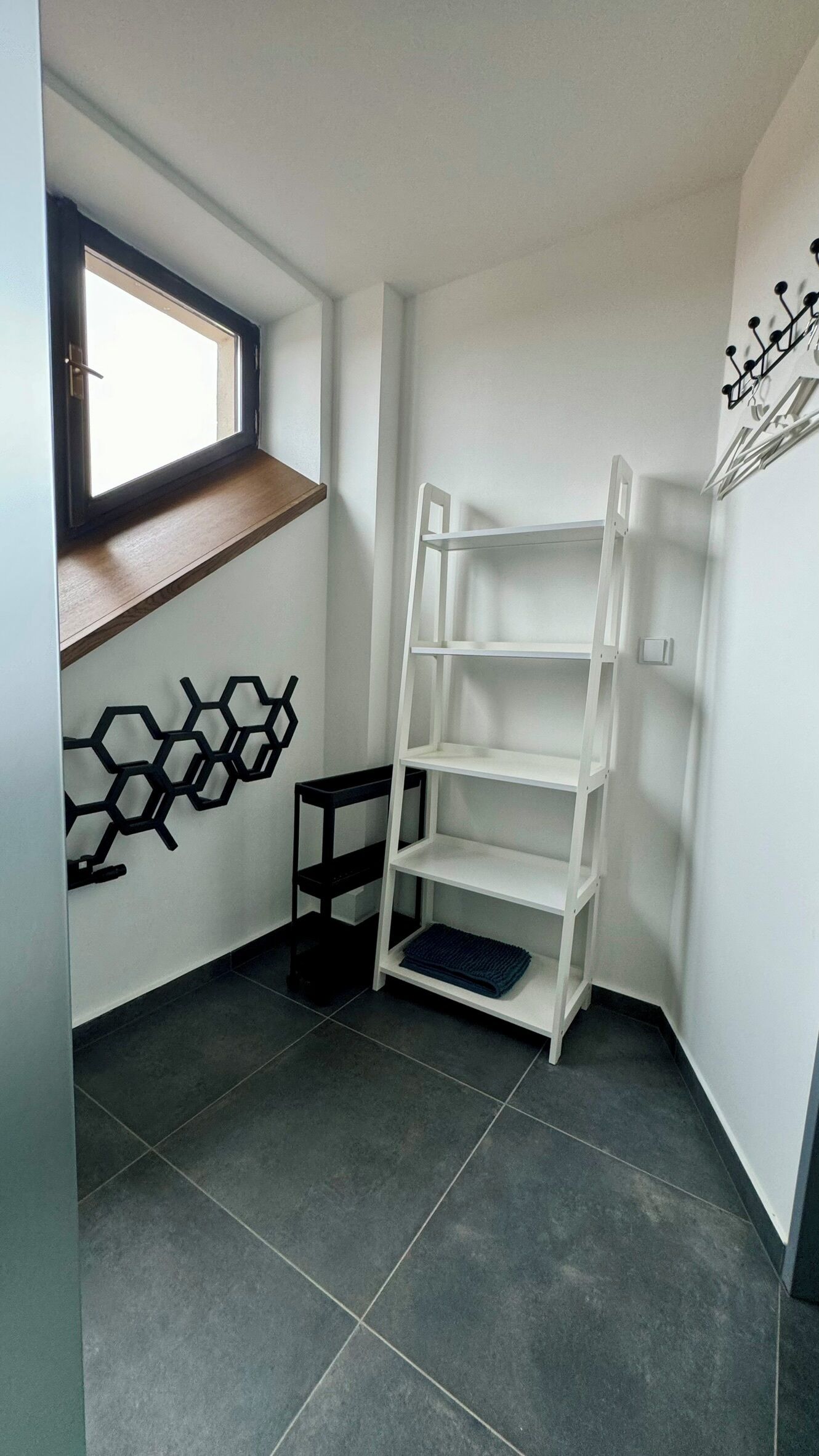 A corner room with a white shelving unit, a small table, and a window with a view.
