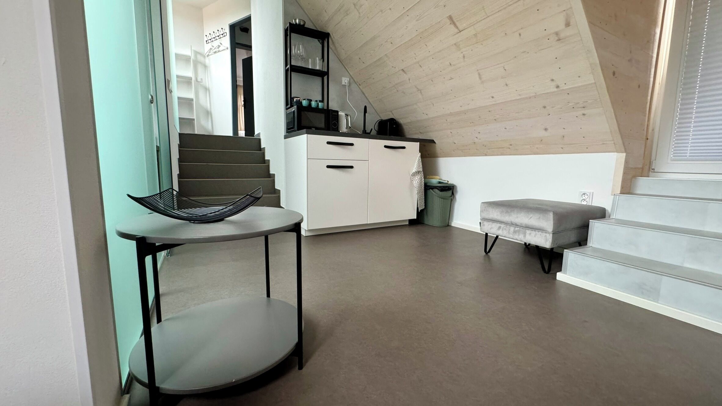 A modern kitchen with white cabinets, a black countertop, and a staircase leading to an upper level.