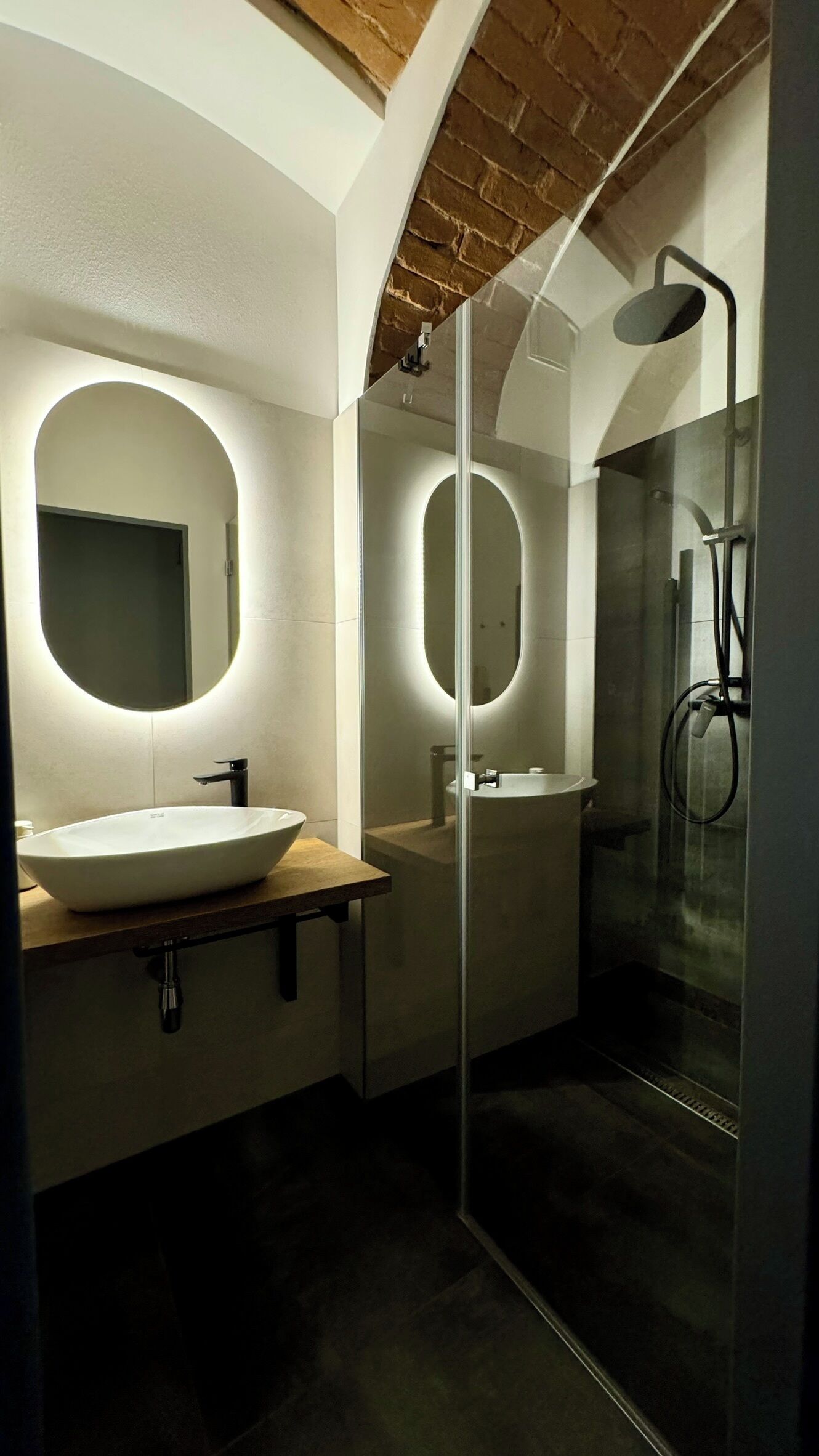 A modern bathroom with a large oval sink, a glass-enclosed shower, and a mirror with a circular light.
