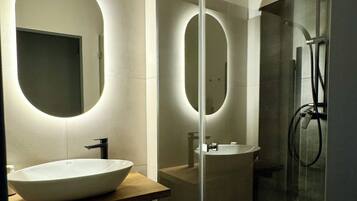 A modern bathroom with a large oval sink, a glass-enclosed shower, and a mirror with a circular light.