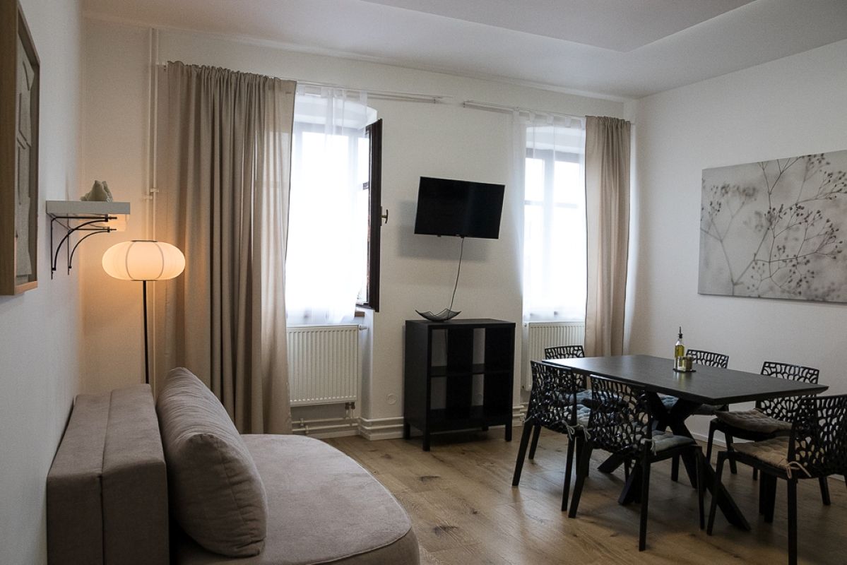 Una sala moderna con sofá, mesa de comedor, sillas, televisor y lámpara.