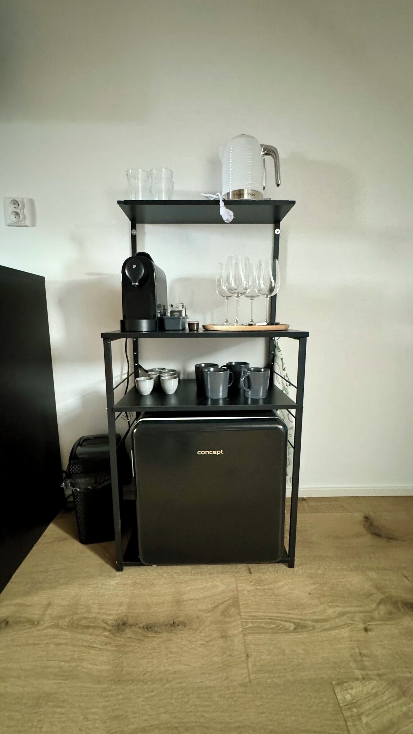 A black kitchen island with a coffee maker, cups, and wine glasses.