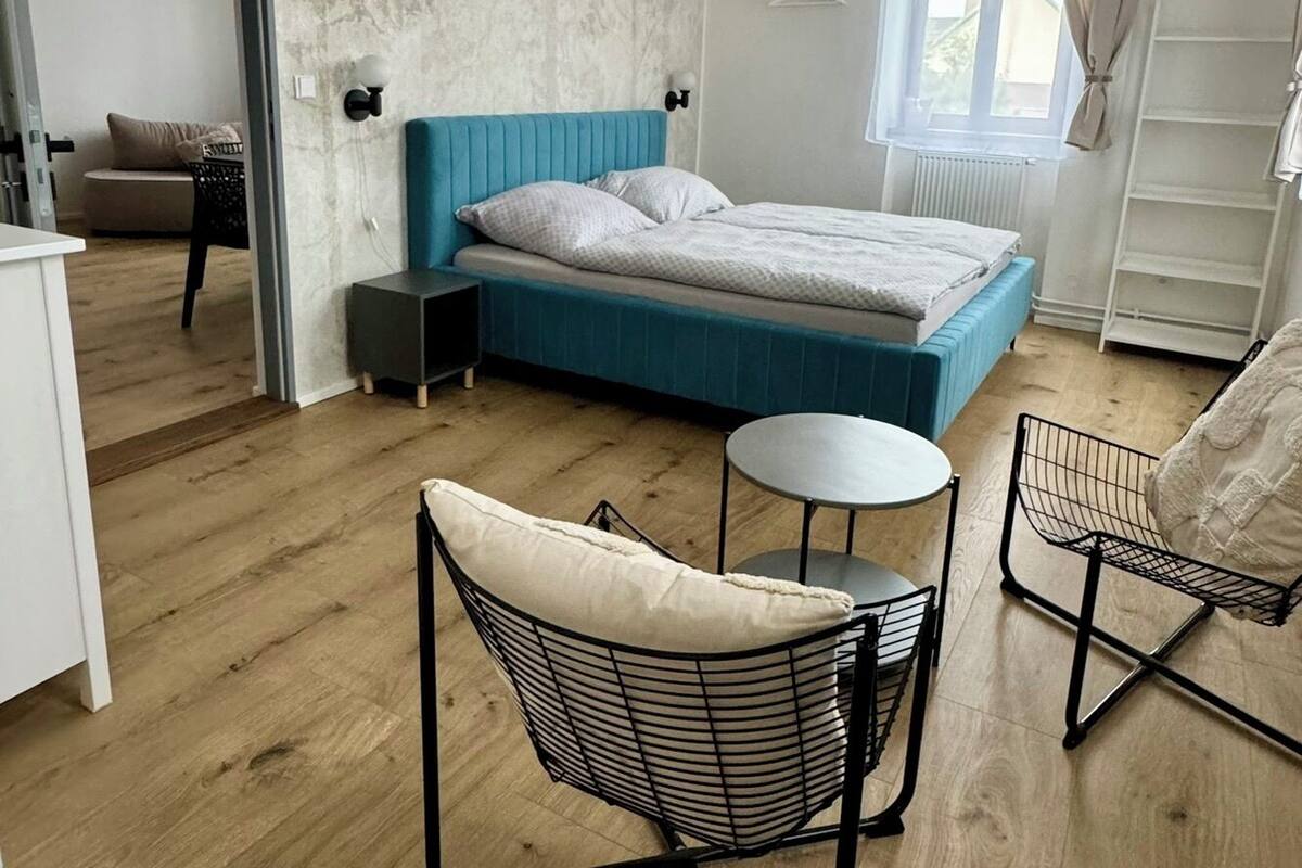 A modern bedroom with a blue bed, a small round table, and two chairs.