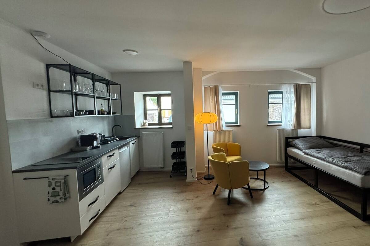 A compact living space with a kitchenette, a single bed, a small table, and a chair.