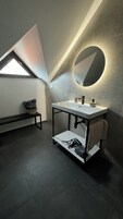 Un baño moderno con tragaluz, un espejo redondo y un lavamanos empotrado.