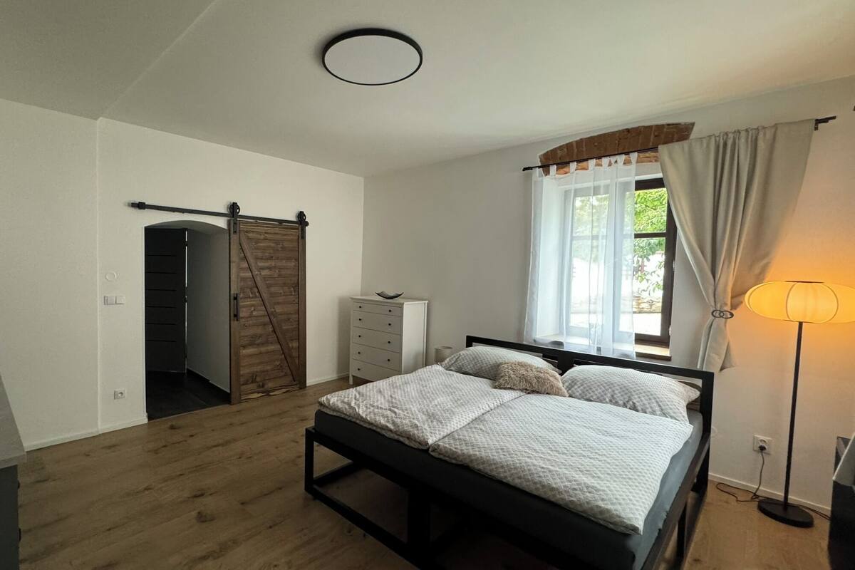 A bedroom with a bed, a dresser, a wardrobe, and a window with curtains.