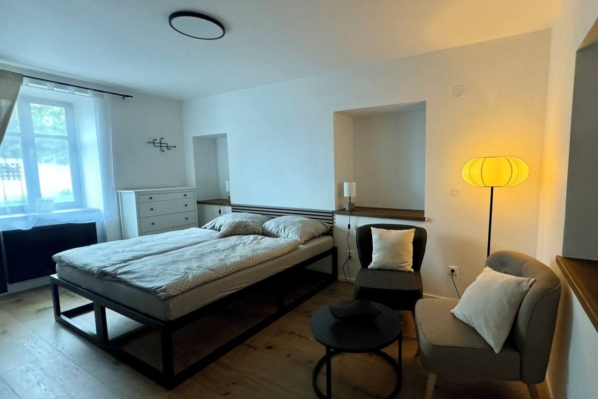 A modern bedroom with a bed, bedside table, chair, and a floor lamp.