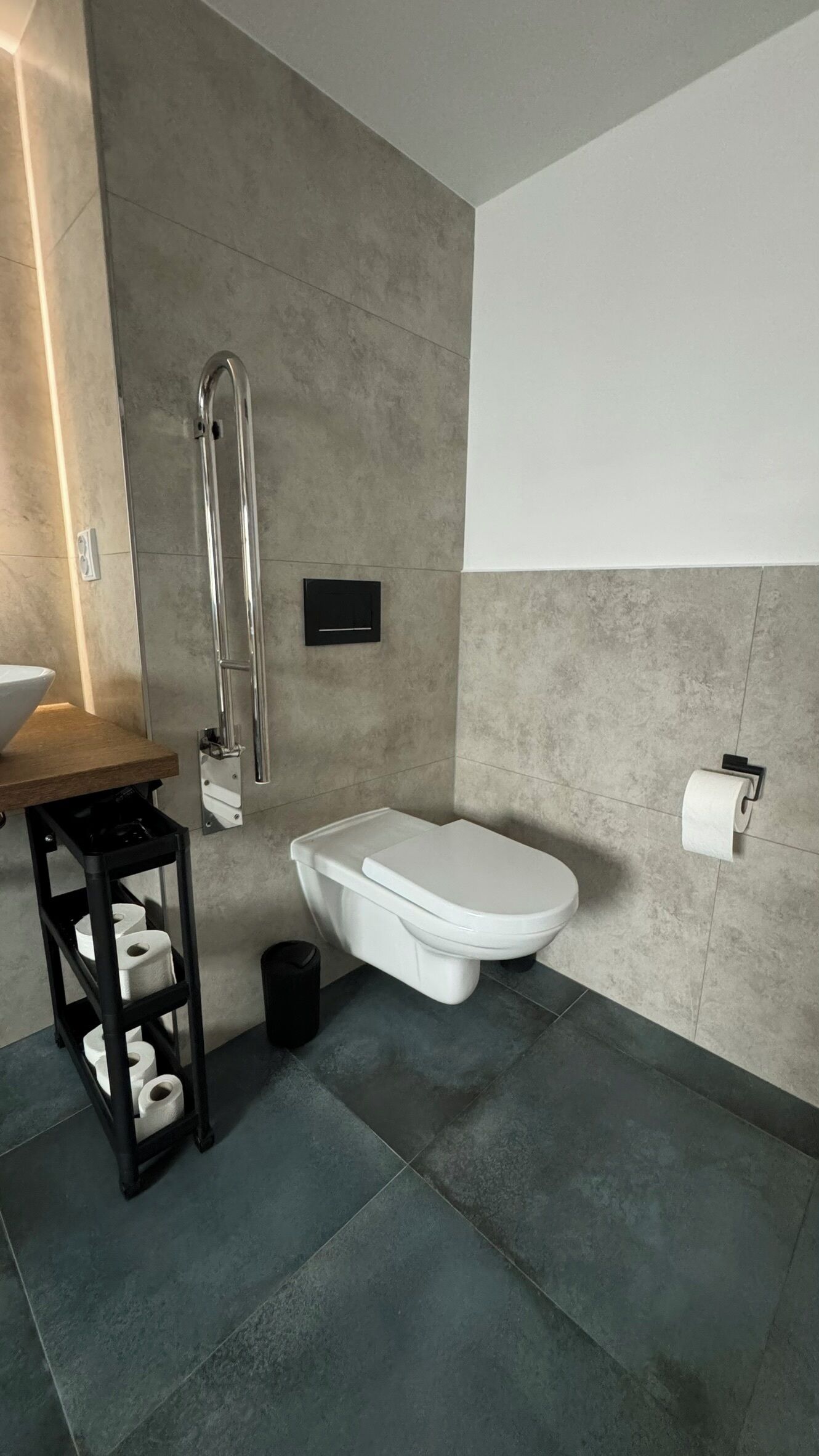 A modern bathroom with a white toilet, a black trash bin, and a shelf with toilet paper.