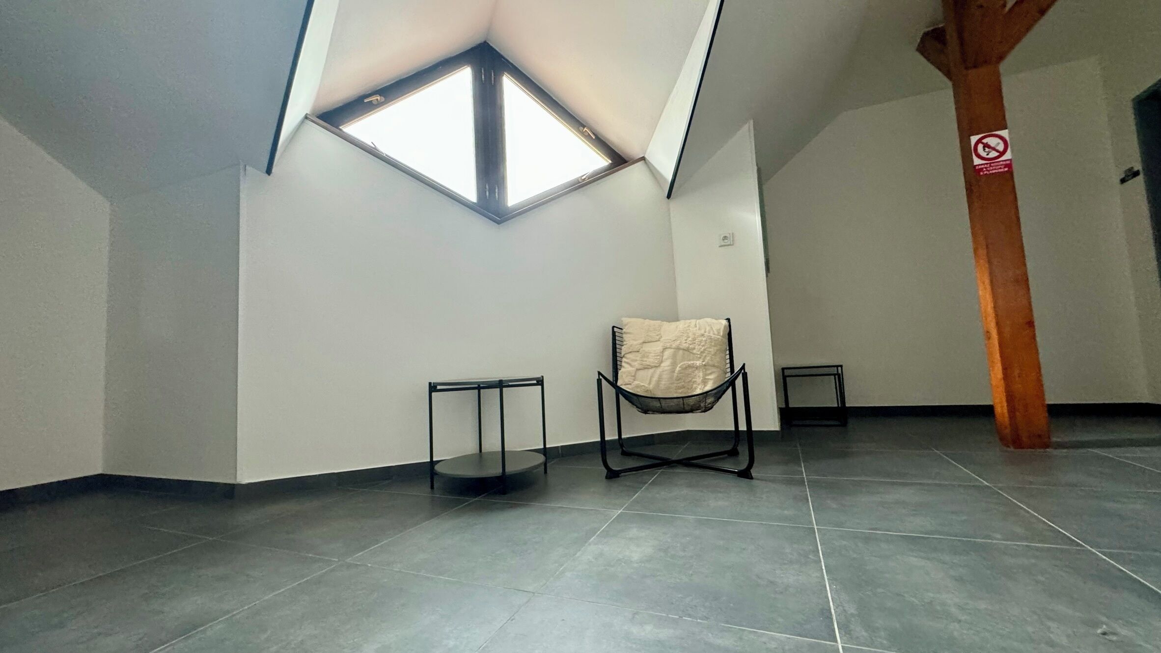 A spacious room with a sloped ceiling, a skylight, and a wooden beam structure.