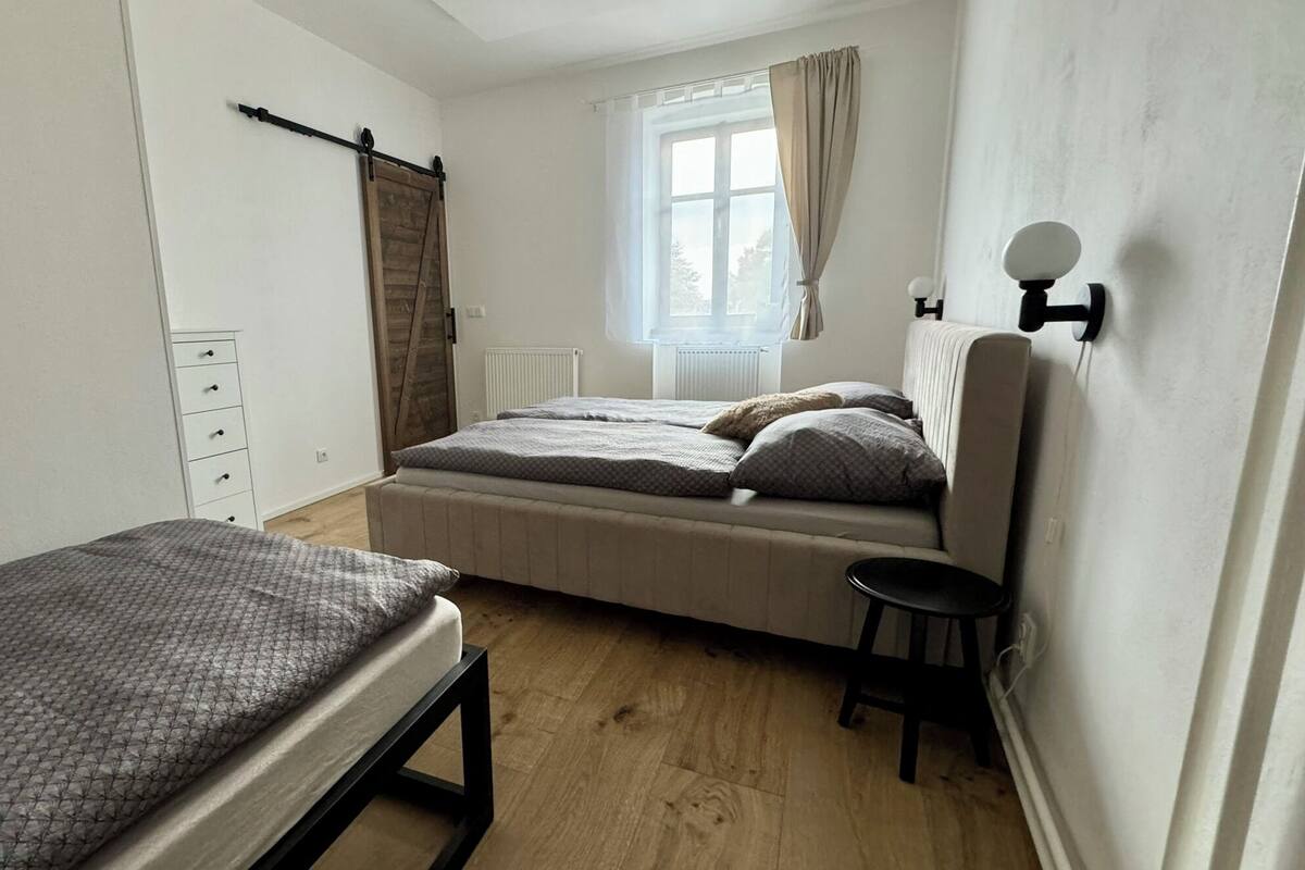 A small, clean room with a bed, a chair, a dresser, and a window with curtains.